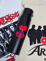 Termo negro de la caja BTS con Tata de BT21 y el logo Arirang, sobre la polera blanca y el totebag con las siluetas de los siete