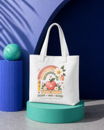 Bolsa tote blanca con el diseño del arcoíris y la manzana «Enseñar, amar, inspirar» estampado