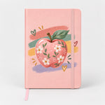 Libreta rosada de tapa dura con una manzana llena de flores sobre pinceladas de colores