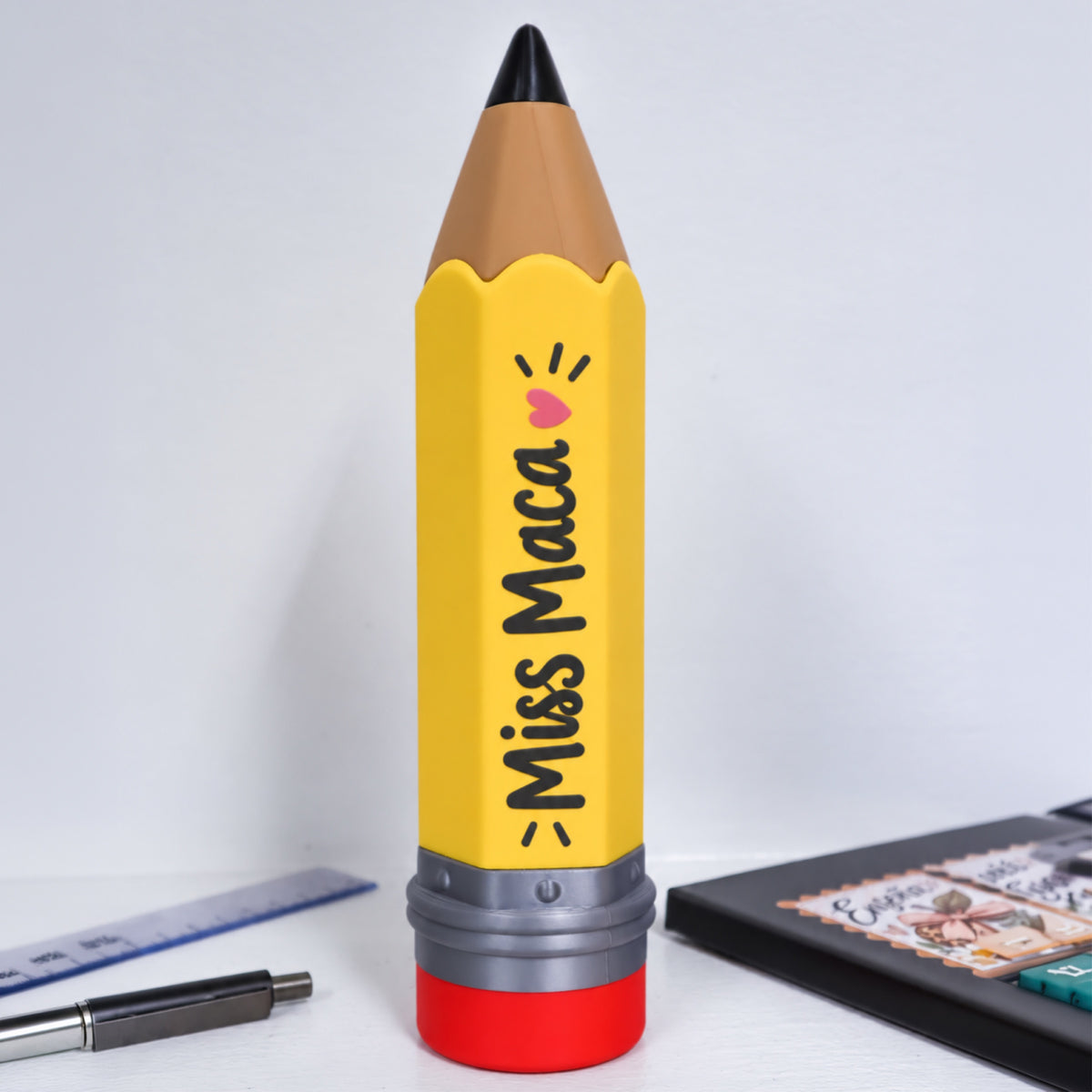Portalápices con forma de lápiz personalizado con el nombre «Miss Maca» escrito a lo largo del cuerpo, con un corazón