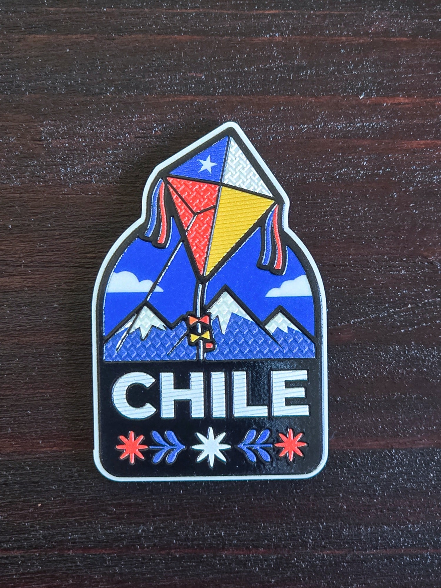 Imán de volantín tricolor entre montañas con la palabra Chile